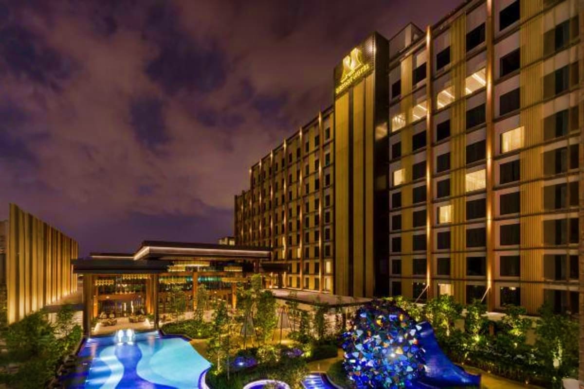 Modern luxury hotel resort at twilight with illuminated gold-toned buildings surrounding a lit blue swimming pool and courtya