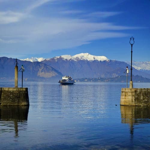 Snow-capped mountain overlooking calm lake with ferry boat and stone pier with lamp posts in foreground at Nainital
