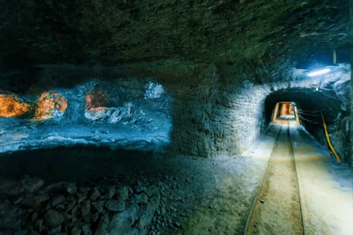 Underground salt mine tunnel in Austria with illuminated tracks and mining cart, showing colorful mineral deposits on tunnel 