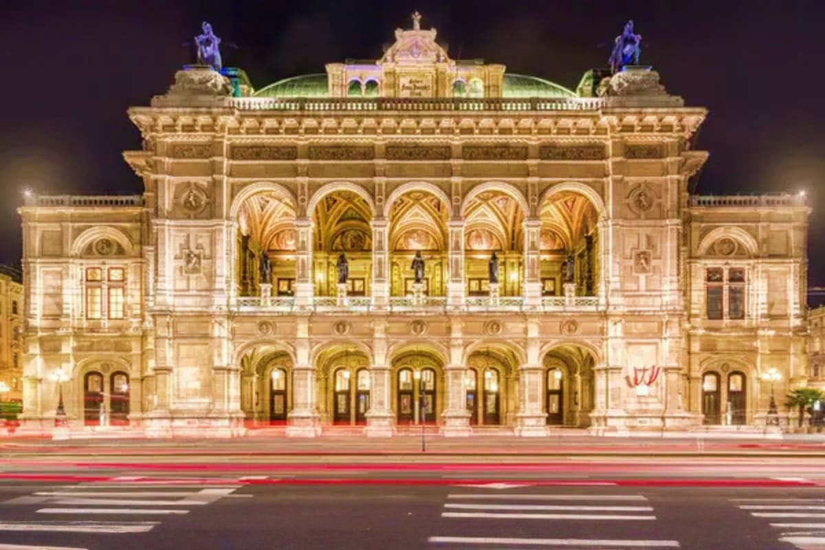 Vienna State Opera House illuminated at night with ornate Renaissance Revival architecture and traffic lights streaking acros