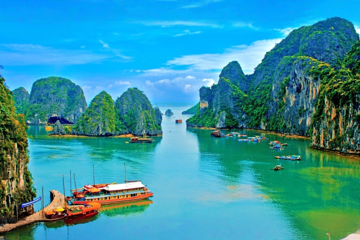 Halong Bay with traditional wooden boats and limestone karst formations rising from turquoise water under blue sky
