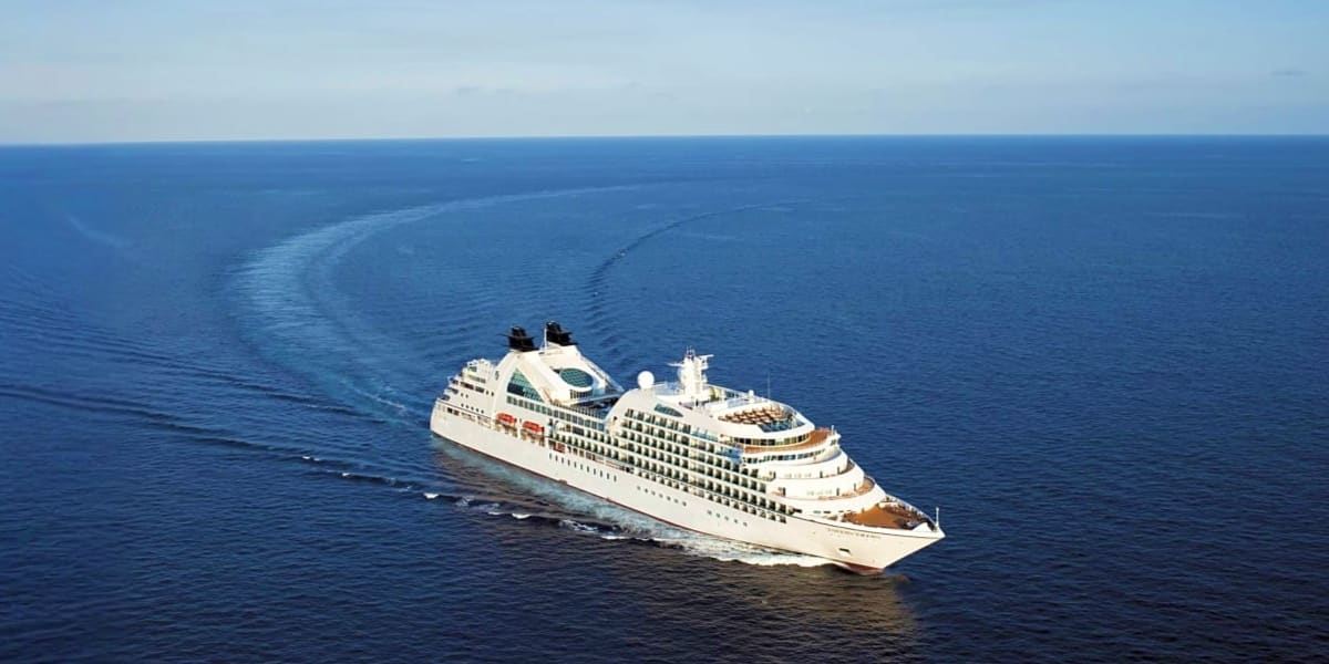 Large luxury cruise ship sailing on calm blue ocean waters with wake trails visible behind it