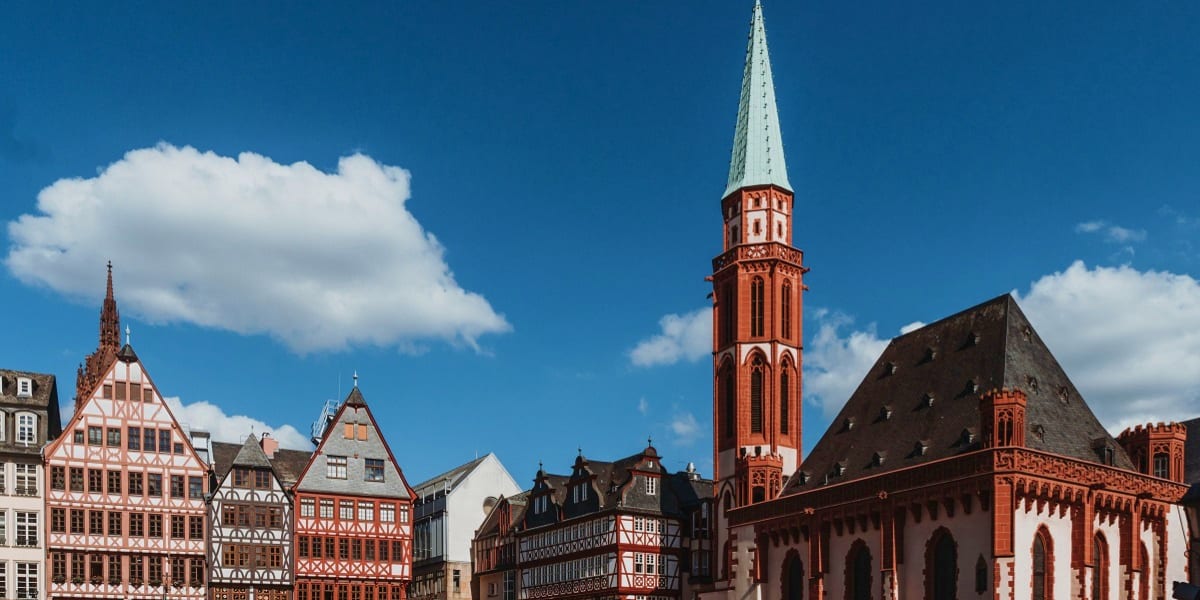 Historic Frankfurt skyline featuring traditional half-timbered buildings and red brick church with tall spire under blue sky