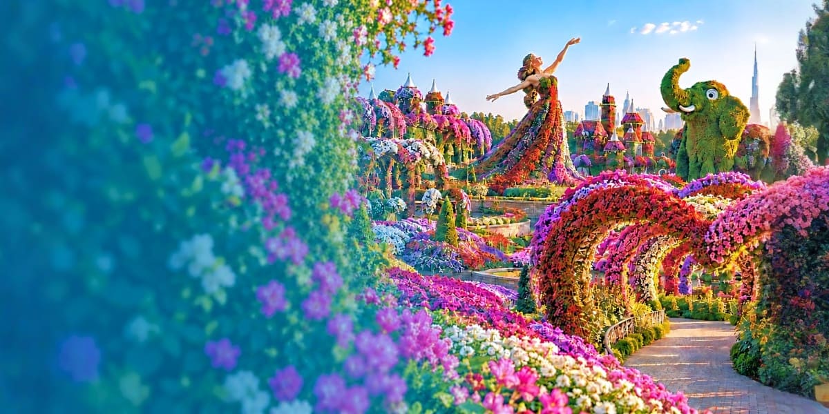 Colorful flower garden pathway with topiary sculptures and Dubai skyline in background at Miracle Garden