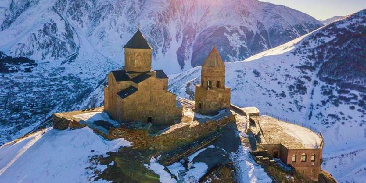 Metekhi Church with twin stone towers surrounded by snow-covered mountains in Georgia's Caucasus region during winter