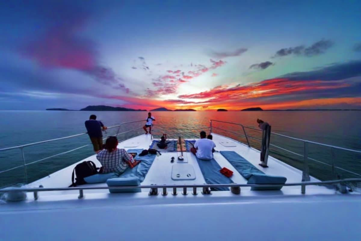 Group of people relaxing on the deck of a boat during a vibrant sunset over calm ocean waters with islands in the distance