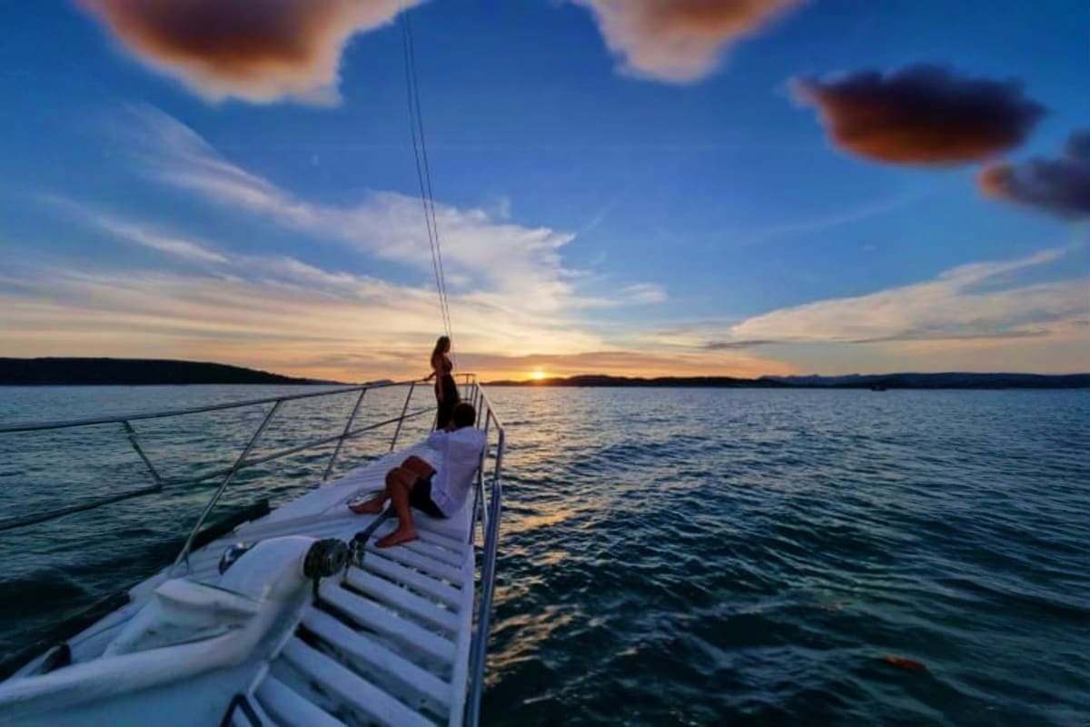 Woman on sailboat bow at sunset with calm water and distant shoreline