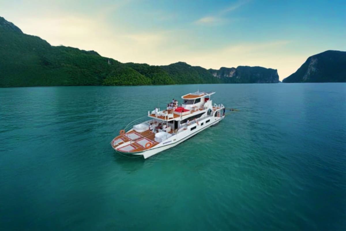 Luxury yacht anchored in turquoise waters surrounded by lush green limestone mountains in tropical bay