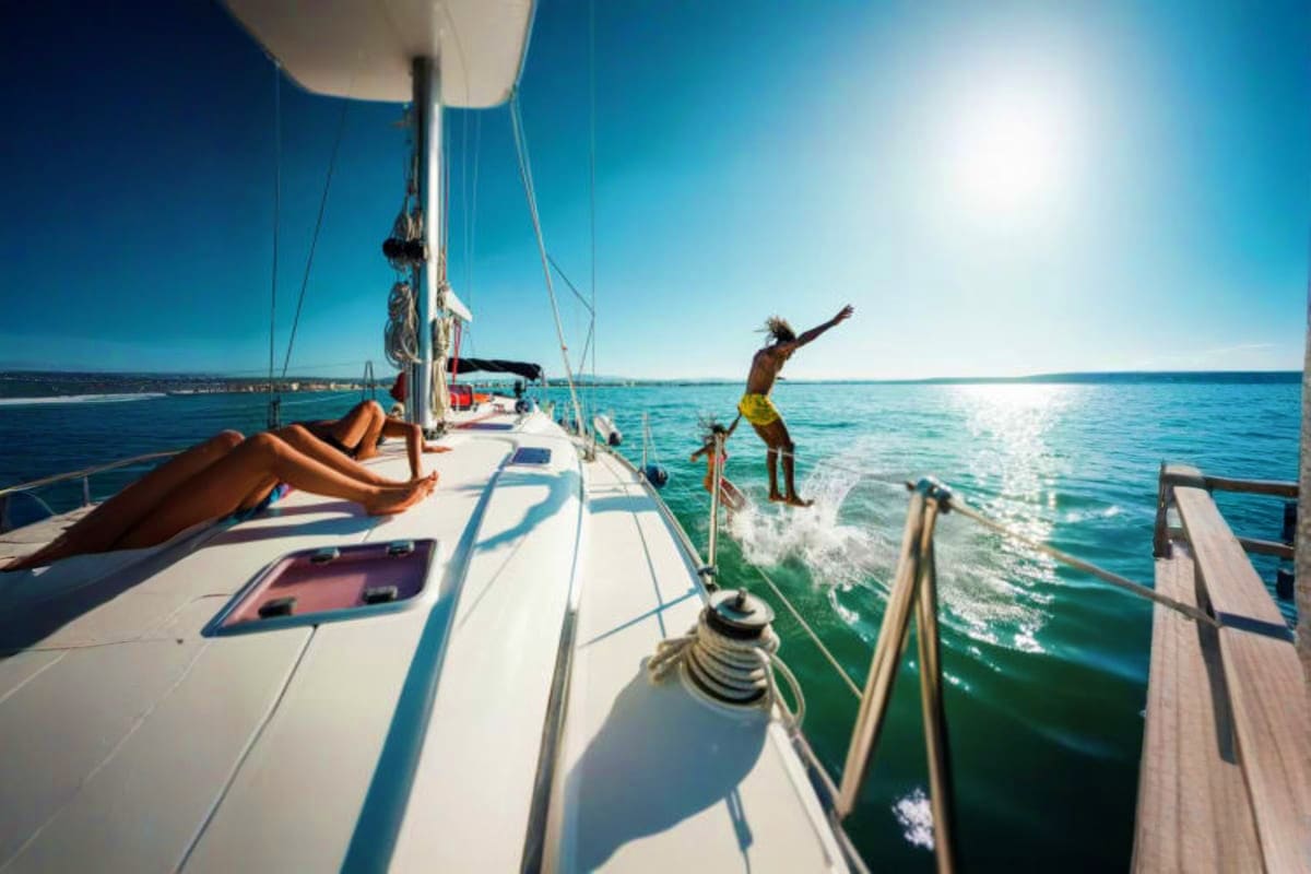 Man jumping off sailboat into turquoise ocean water with passengers relaxing on deck during daytime cruise