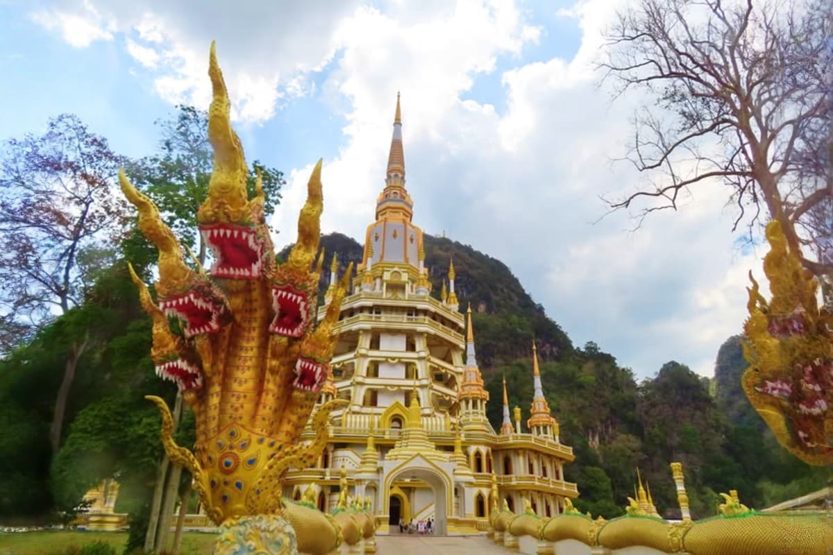Krabi City Tour Golden Buddhist temple with ornate spires and dragon statues nestled against limestone cliffs in Krabi, Thailand