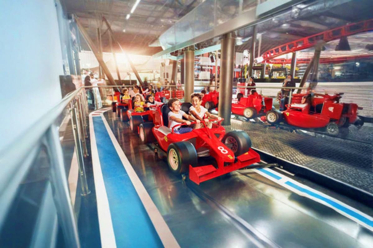 Children riding red Ferrari-themed race car rides at Ferrari World Abu Dhabi indoor attraction with track and spectators