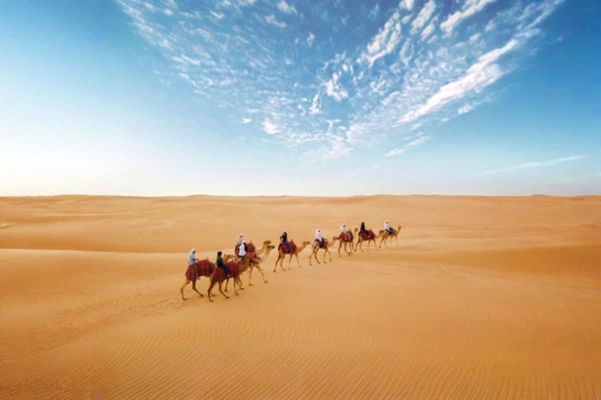 Camel Riding Caravan of tourists riding camels across vast sand dunes under clear blue sky