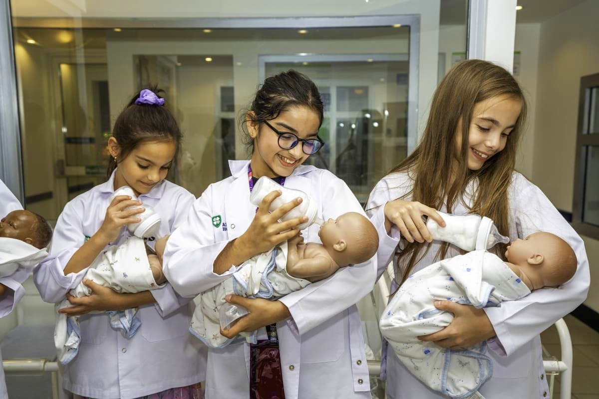 Dubai Mall Kidzania Young girls in white lab coats holding baby dolls at Kidzania Dubai, a children's role-play activity center