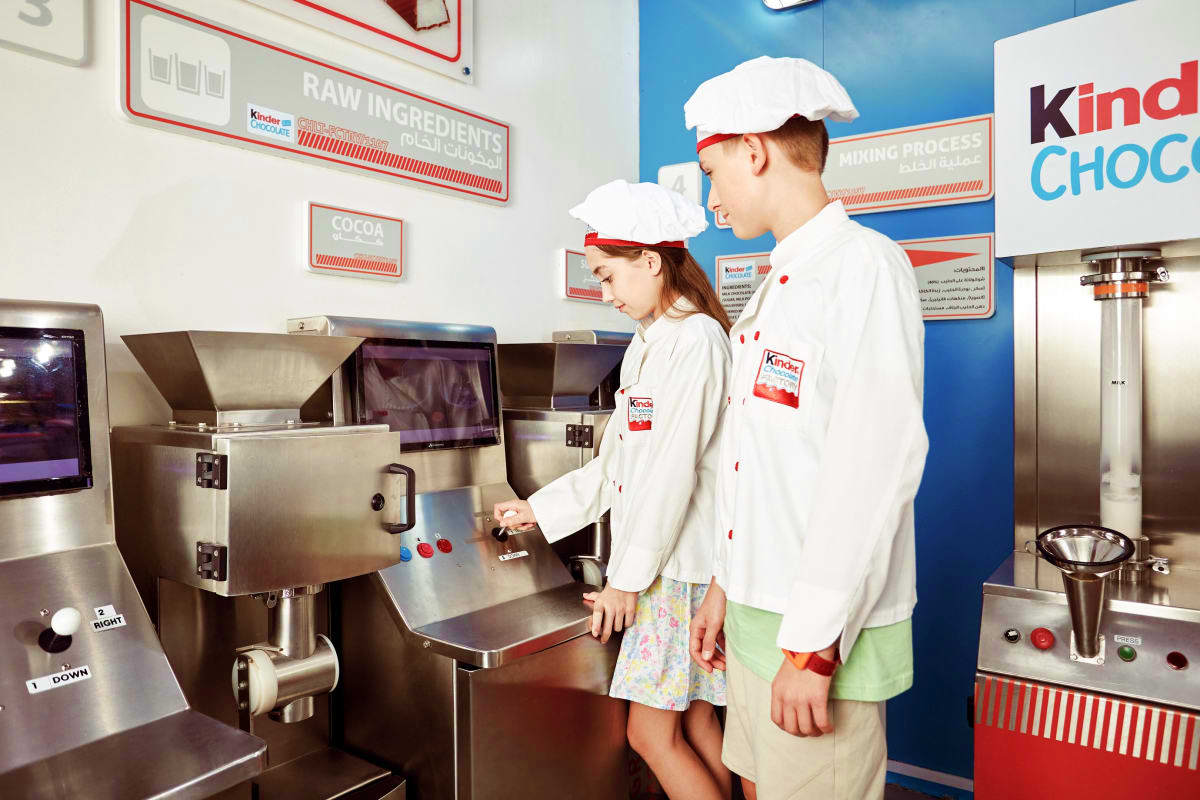 Dubai Mall Kidzania Two children in chef uniforms and white hats operating chocolate-making equipment at KidZania Dubai chocolate factory exhibit