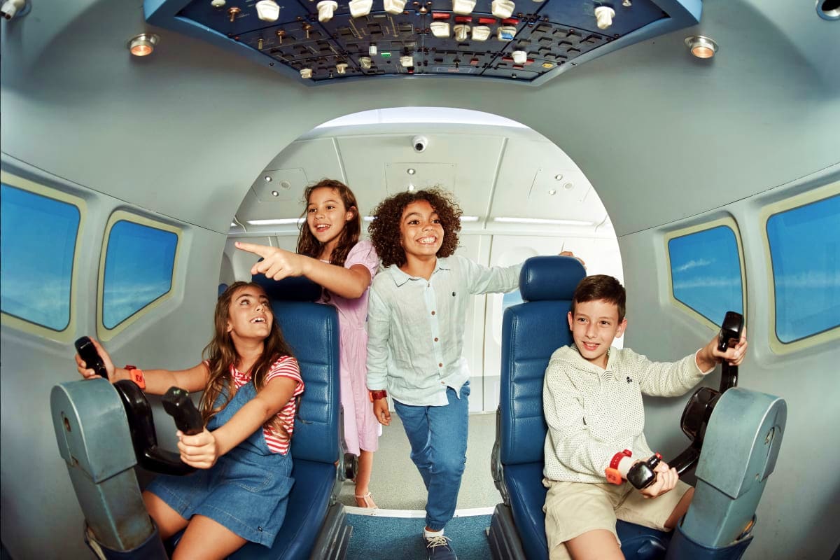 Dubai Mall Kidzania Four children playing video games inside a small aircraft cabin simulator at Kidzania Dubai