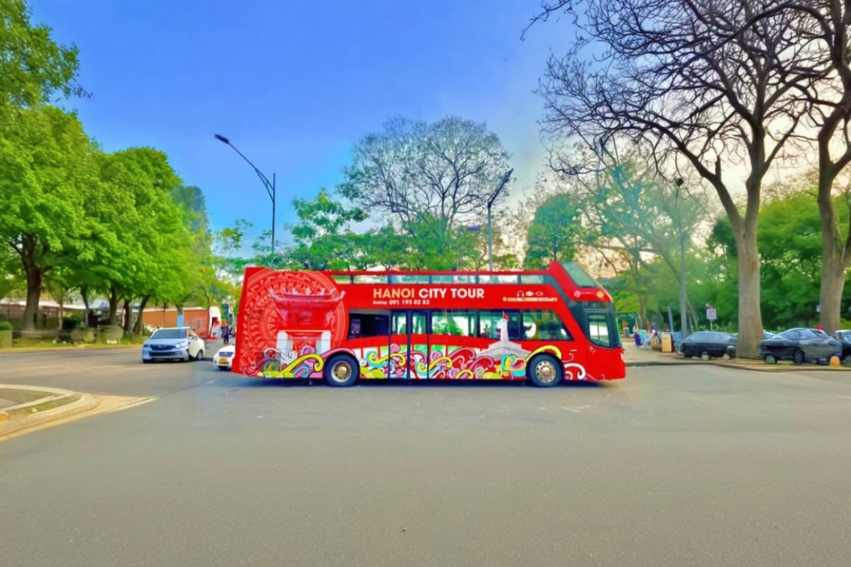 Red double-decker Hanoi City Tour bus parked on street with trees and buildings in background