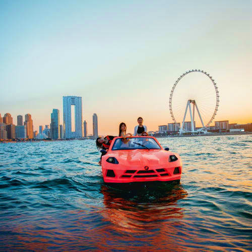 Red sports car floating in water with Dubai skyline and Ferris wheel at sunset