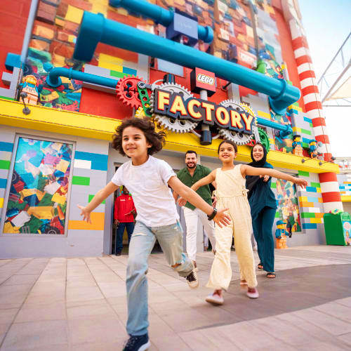 Family running outside colorful LEGO Factory building at Legoland Dubai with bright red, yellow, and blue brick-patterned fac