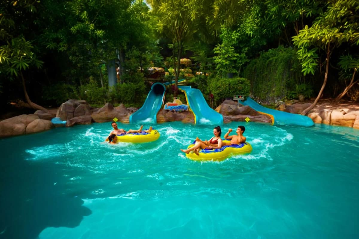 Children on yellow inflatable tubes in turquoise water pool with blue water slides and lush green trees at Sunway Lagoon them