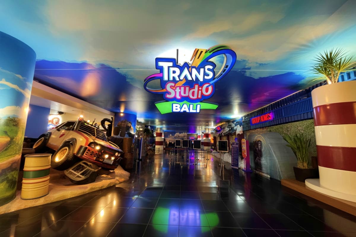 Trans Studio Bali theme park entrance with colorful logo, indoor corridor displaying car displays and attractions with neon l