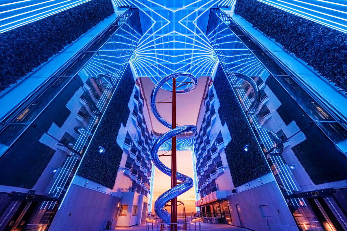 MSC World Europa Barcelona Roundtrip Cruise Modern architectural courtyard with symmetrical blue neon lighting, towering buildings, and spiral staircase at sunset on MSC