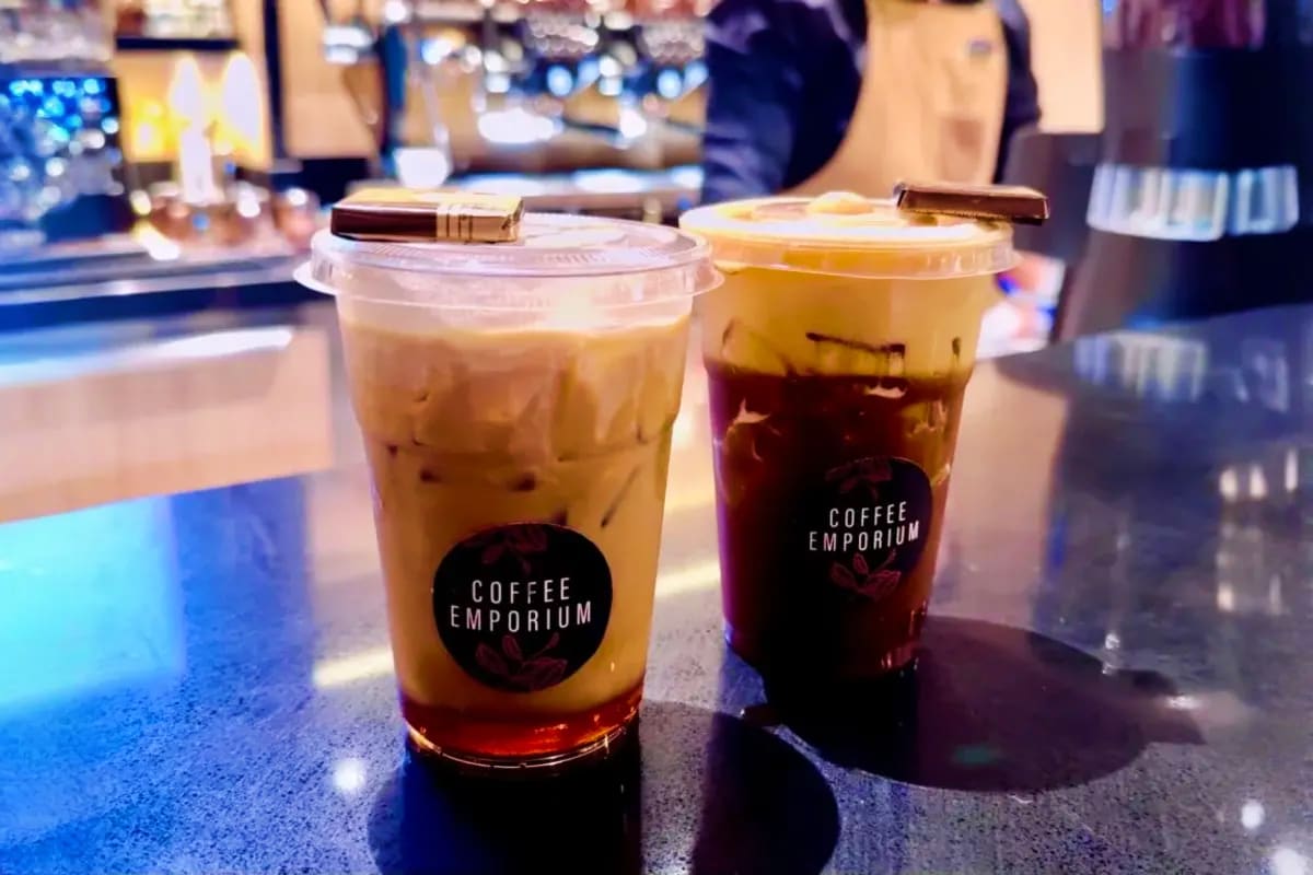 Two iced coffee drinks with Coffee Emporium branding on a cruise ship counter with blurred background