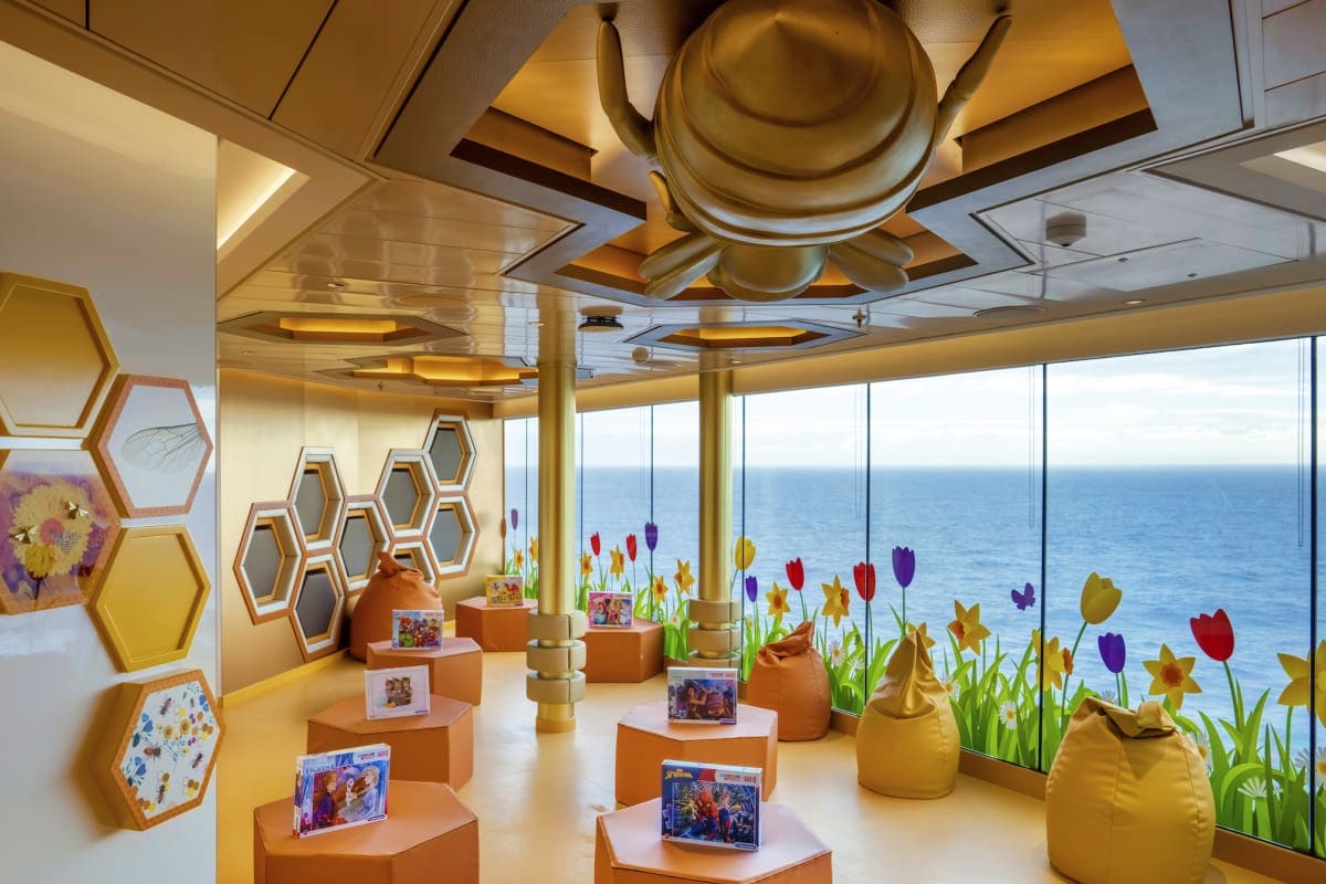 Modern cruise ship interior gallery with orange display pedestals, colorful flower decorations, and panoramic ocean views thr