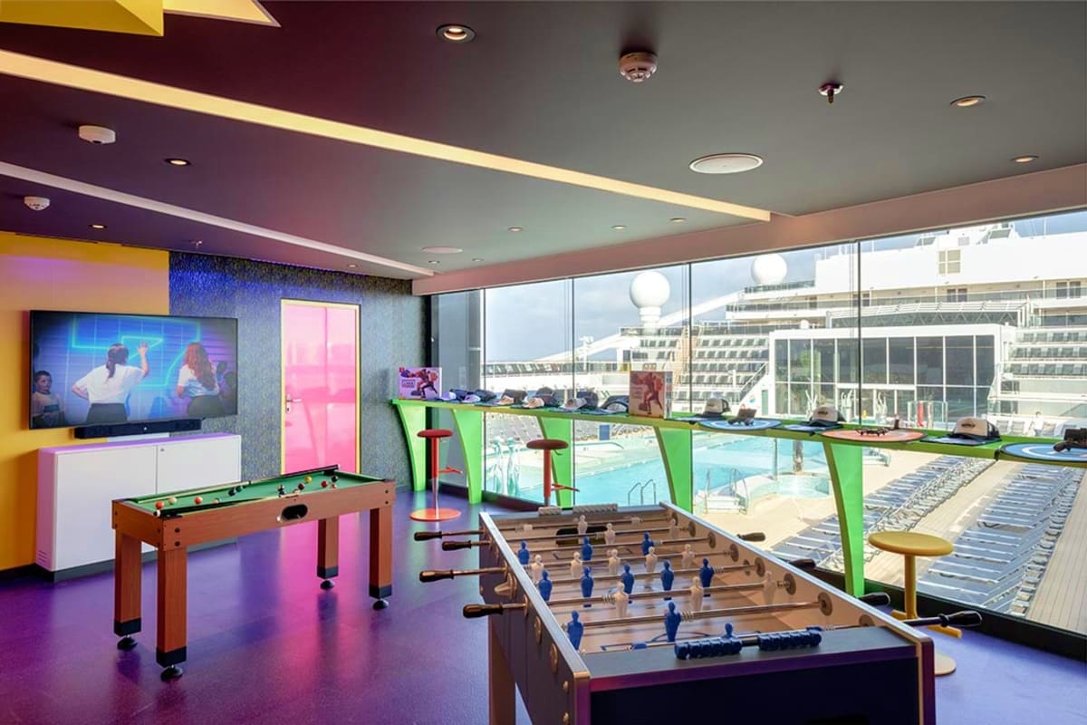 Modern cruise ship game room with pool table, foosball table, flat-screen TV, and floor-to-ceiling windows overlooking the oc