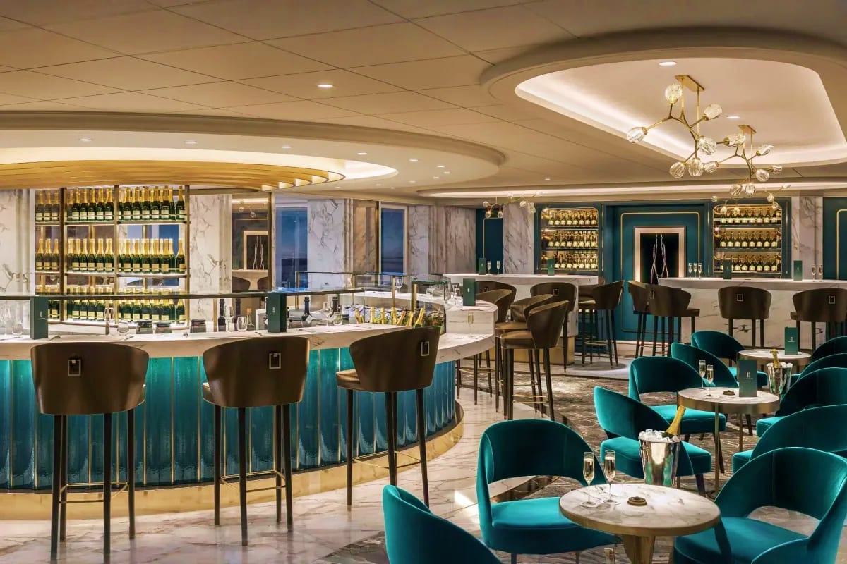 Elegant cruise ship bar and lounge with teal velvet seating, marble accents, and illuminated wine displays behind curved coun