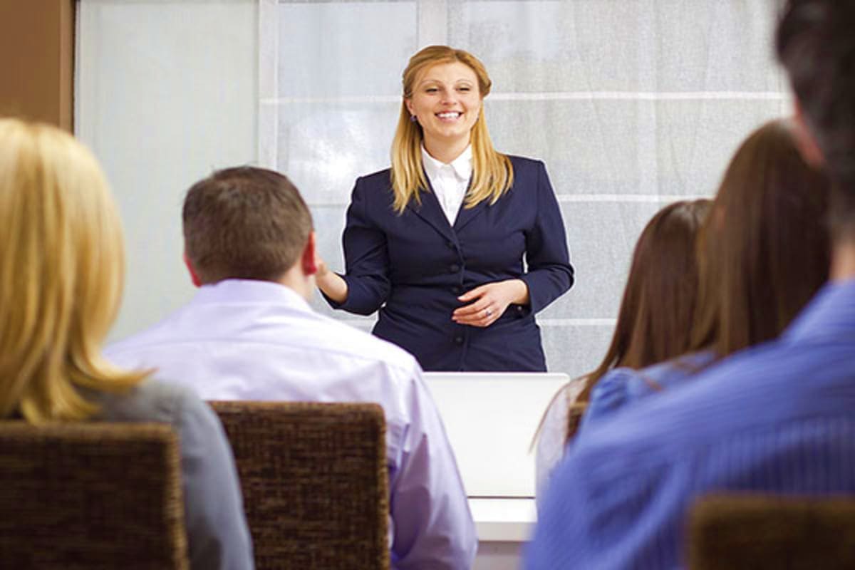 Professional woman in navy blazer presenting to business colleagues in modern office conference room