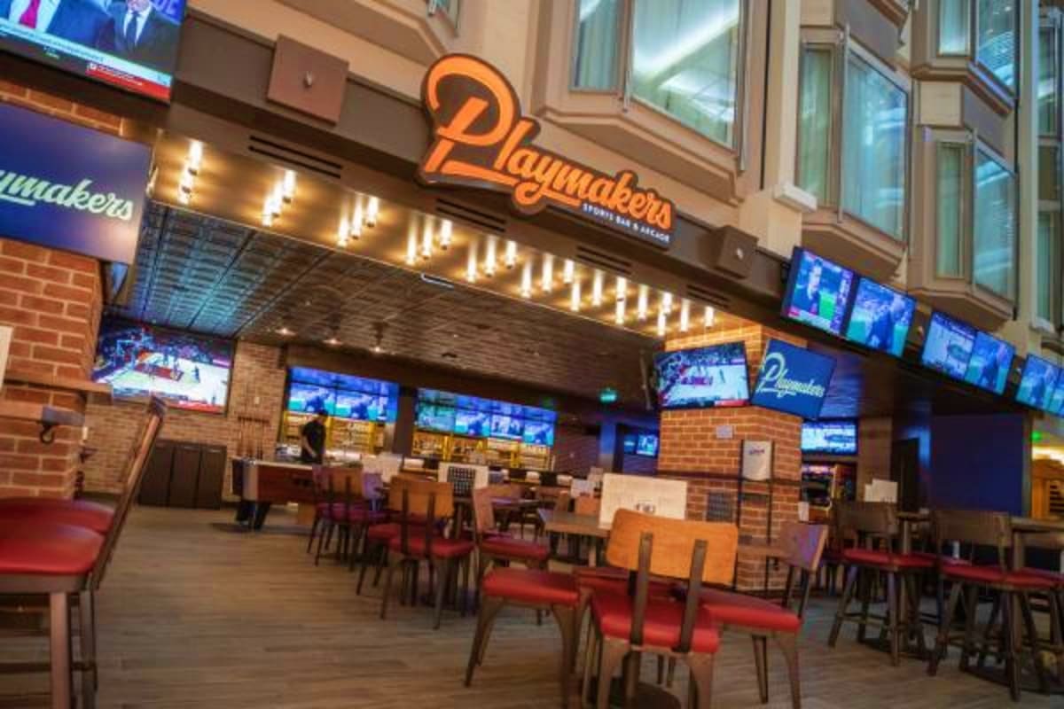 Playmakers sports bar and restaurant interior with orange neon sign, multiple TV screens, and red seating area