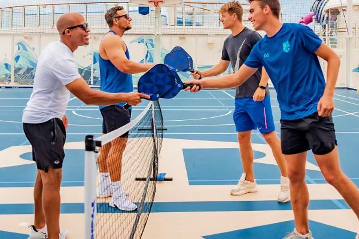 Group of men playing pickleball on outdoor court with blue and white striped surface near waterfront building