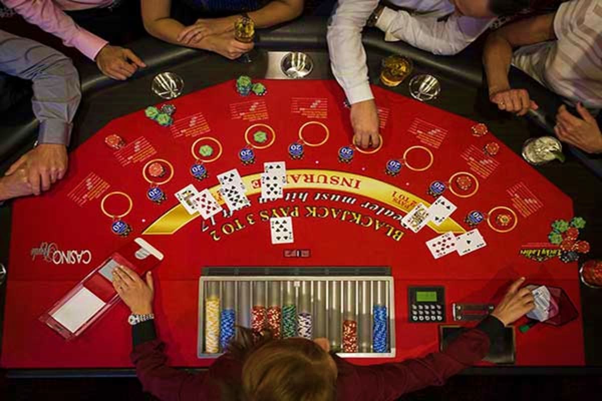 Overhead view of blackjack table with players holding cards and casino chips on red felt surface