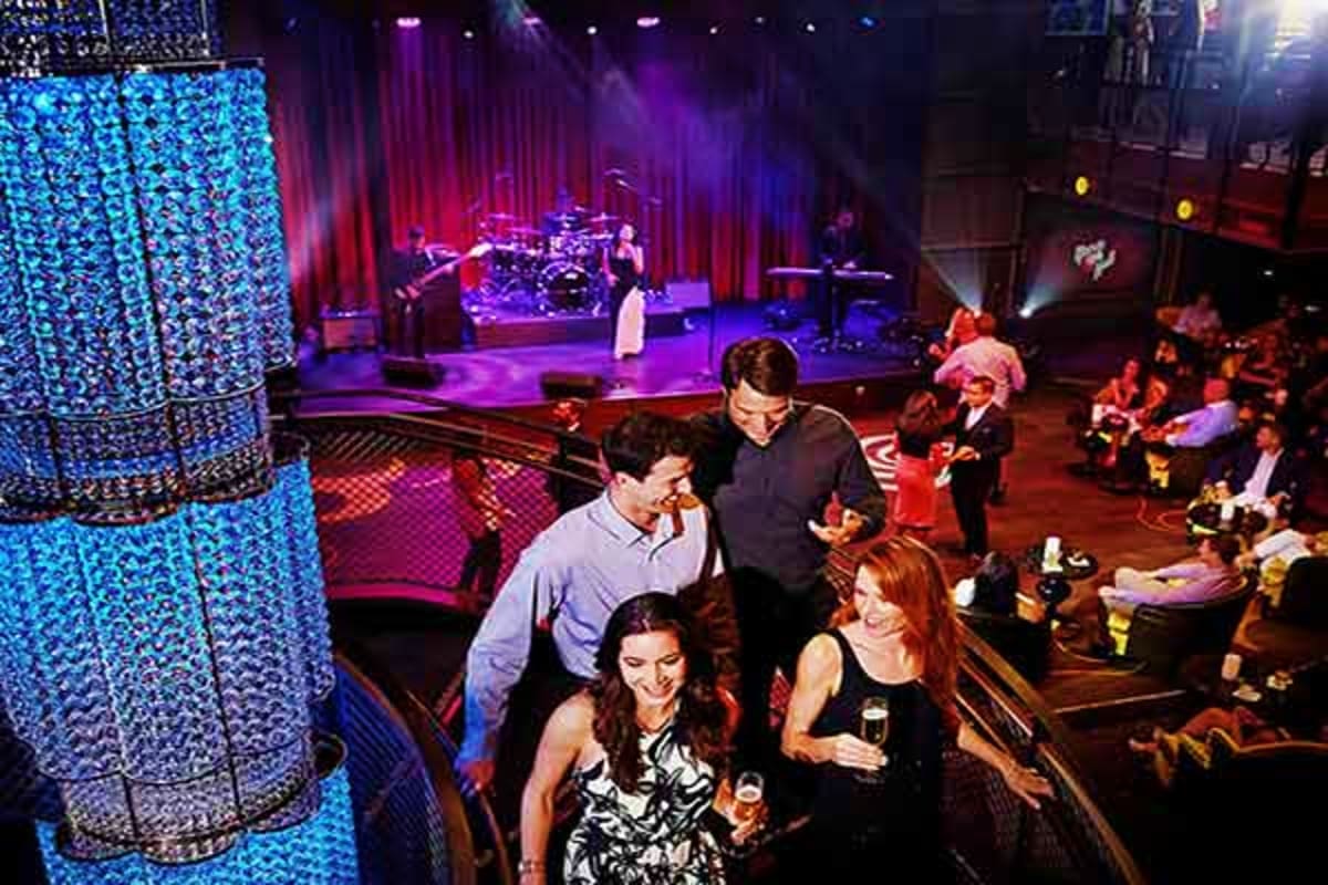 Guests dancing and socializing on a nightclub dance floor with a live band performing on stage under purple and blue stage li