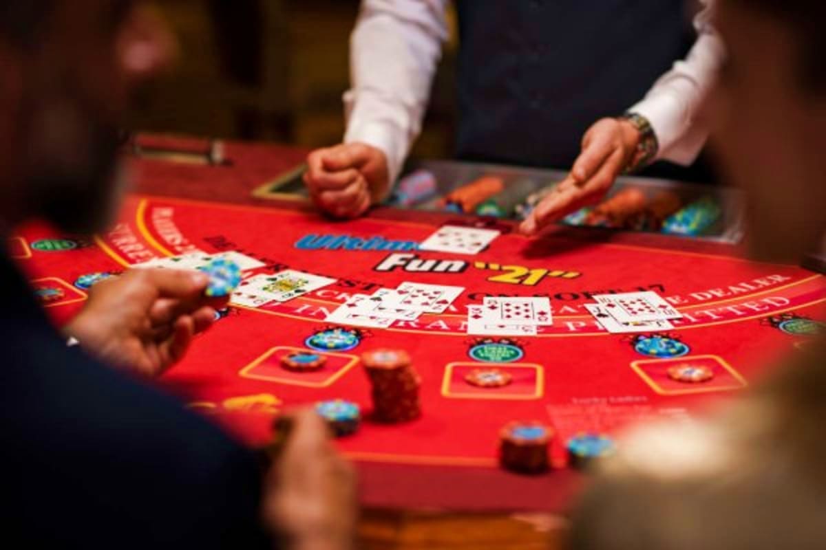 Blackjack table with playing cards and poker chips on red felt, dealer and players' hands visible during casino gaming