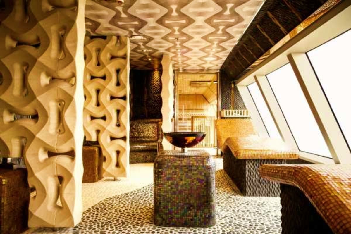 Luxury cruise ship spa hallway with ornate carved wooden pillars, patterned ceiling, and skylight windows