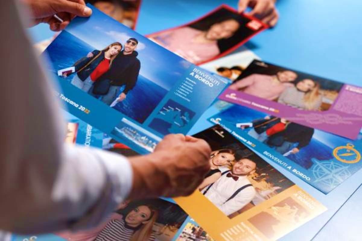 Person holding and reviewing multiple colorful Costa Diadema cruise brochures featuring couple portraits and Mediterranean de