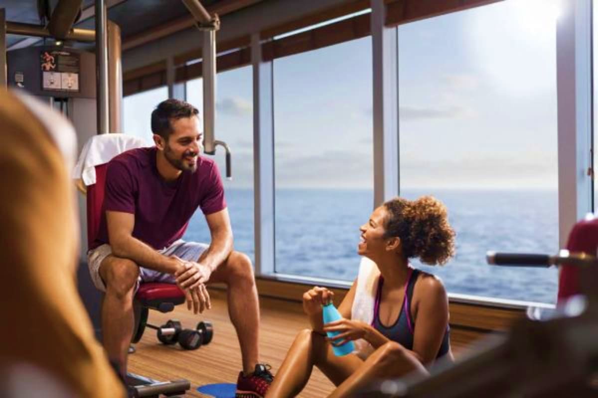 Man and woman talking in a ship's fitness center with ocean views through large windows