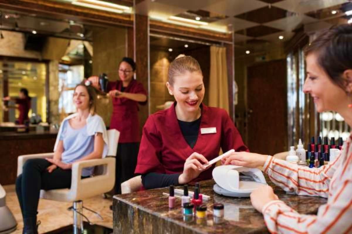 Professional nail technician applying polish to customer at salon counter with staff and clients in background on cruise ship
