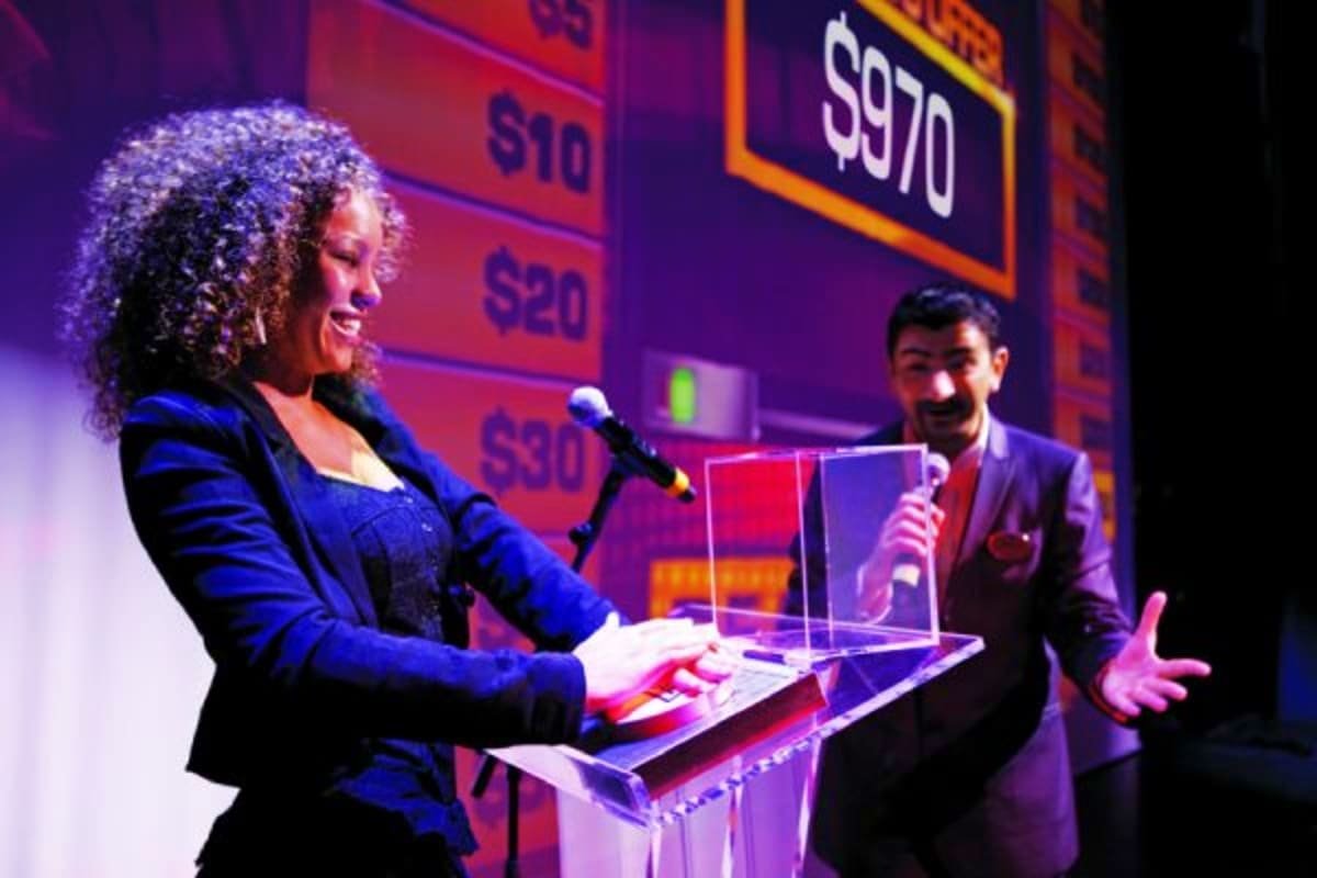 Two hosts on stage at auction event with price board showing amounts up to $970 in background, Norwegian Jade Japan Discovery