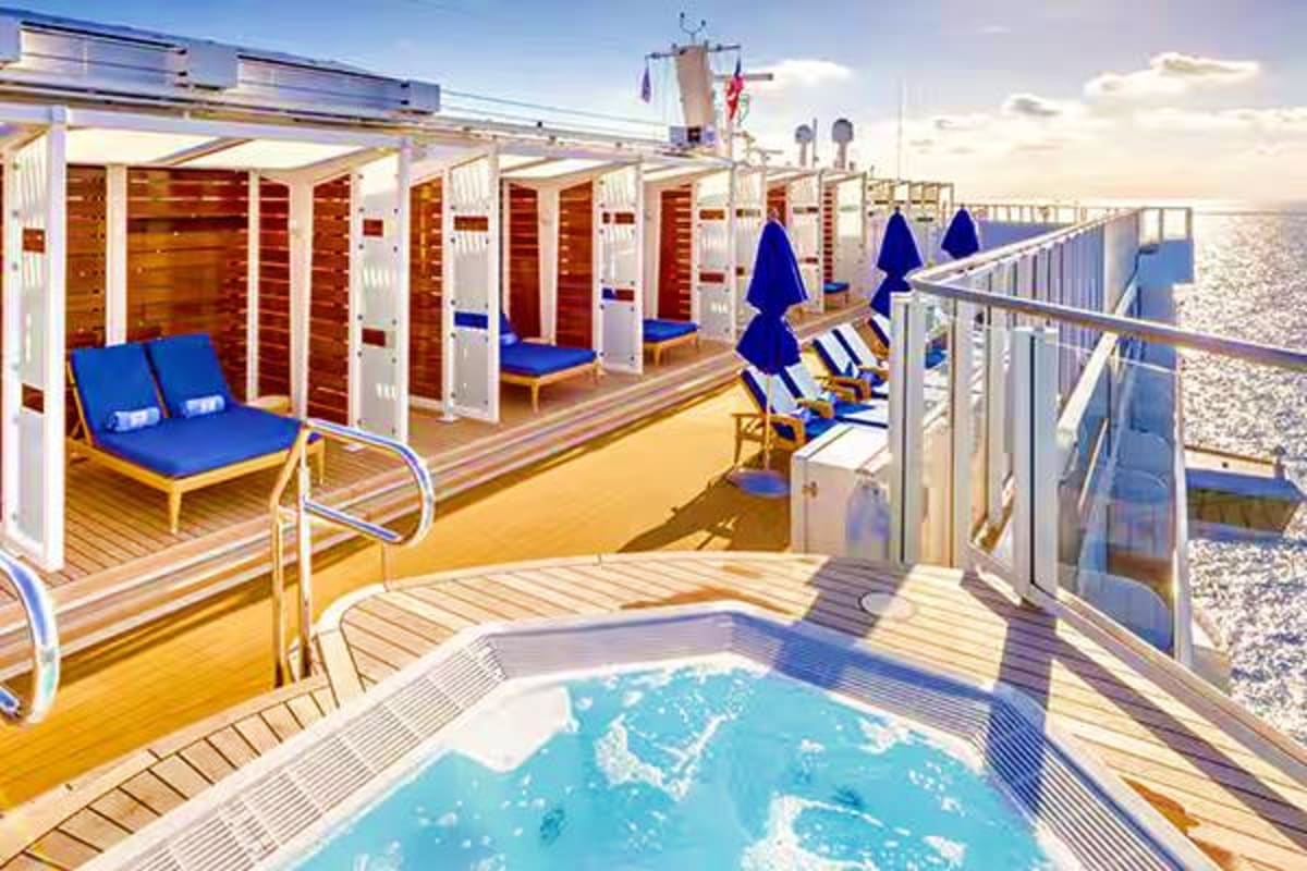 Cruise ship deck with hot tub, lounge chairs, blue umbrellas, cabins, and ocean view on Norwegian Jade