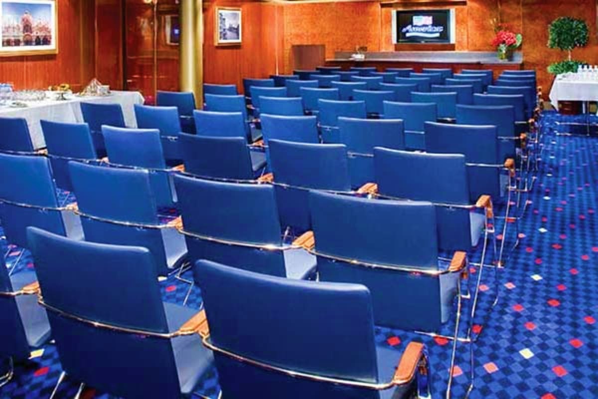 Empty theater auditorium with blue cushioned seats, orange accent walls, and blue patterned carpet inside Norwegian Jade crui