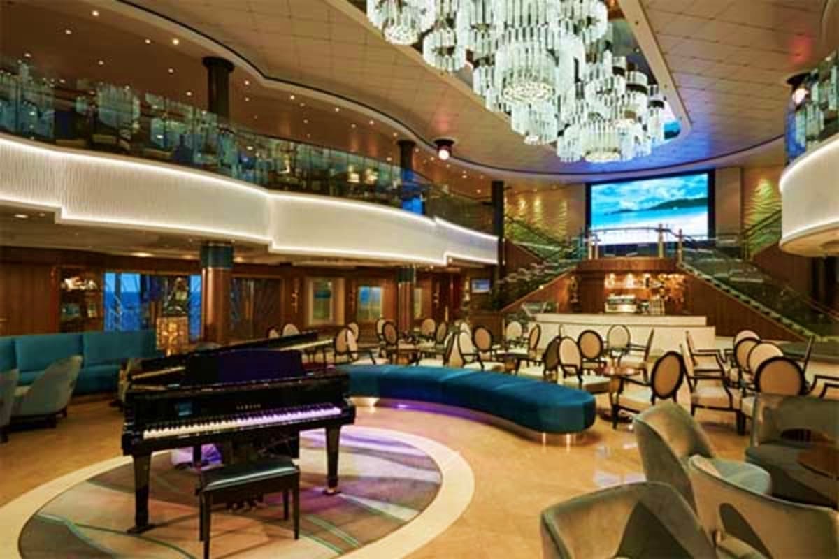 Elegant cruise ship atrium lounge with grand piano, chandelier, curved balconies, and upscale seating areas