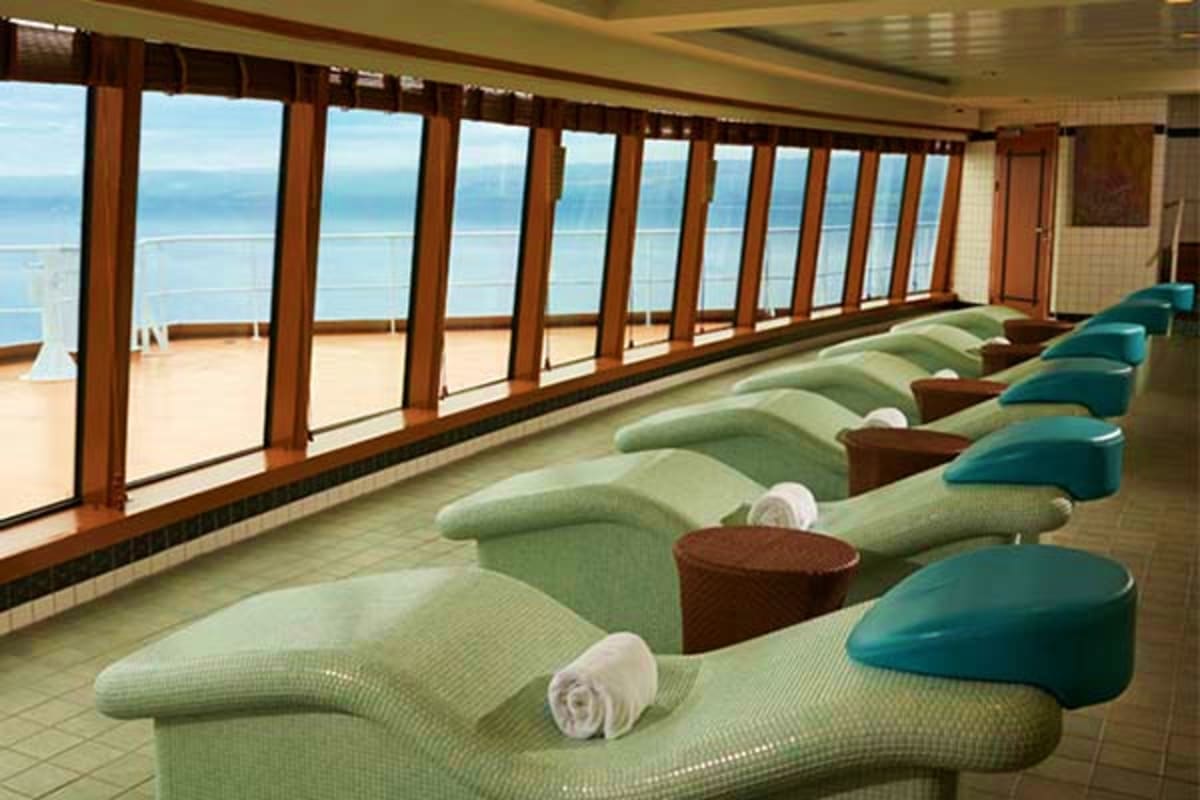 Cruise ship spa relaxation area with lounge chairs overlooking ocean view through floor-to-ceiling windows