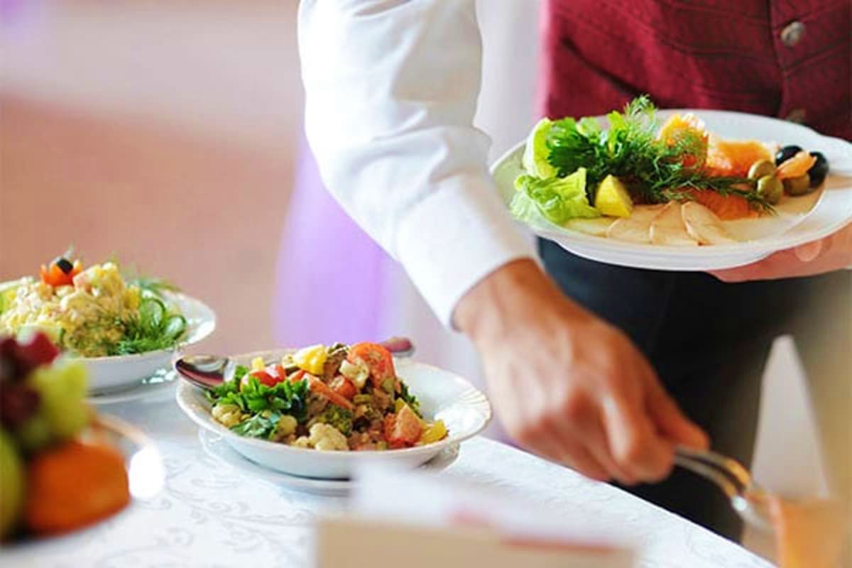 Server holding plates of gourmet Asian cuisine with fresh vegetables and seafood at fine dining restaurant