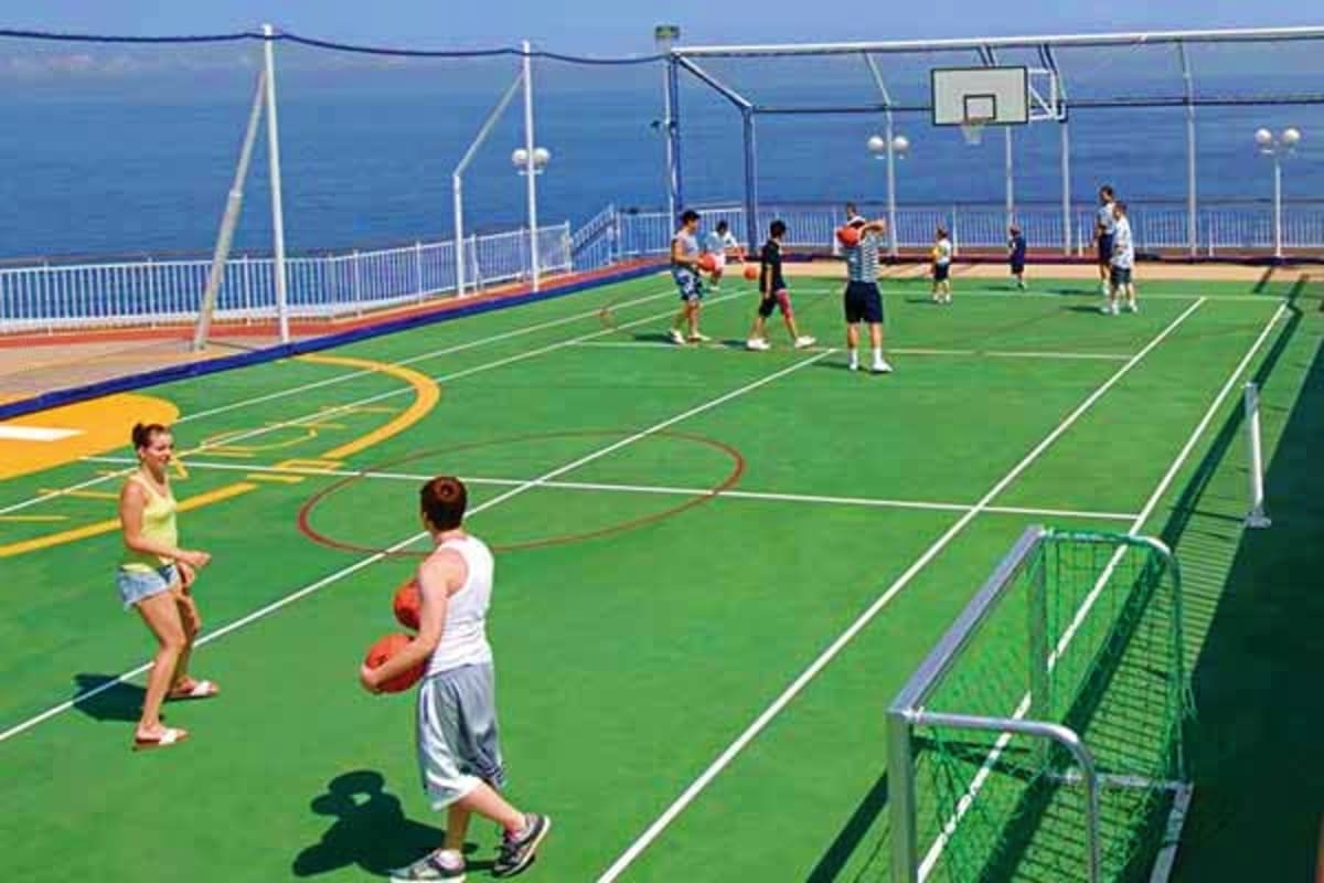 Passengers playing basketball and other sports on the outdoor deck of a cruise ship with ocean views in the background