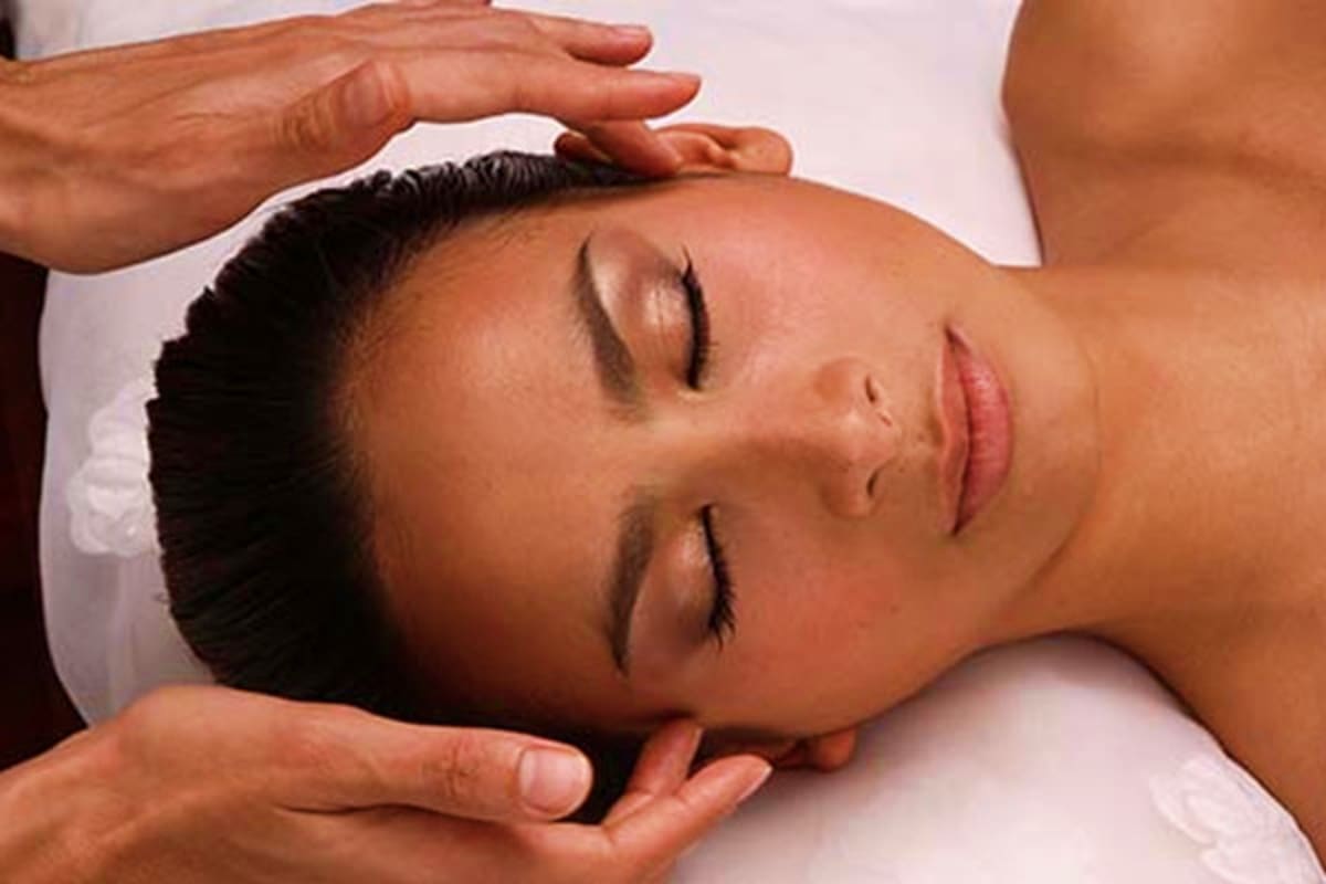 Woman receiving relaxing spa massage treatment with therapist's hands on her head and shoulders