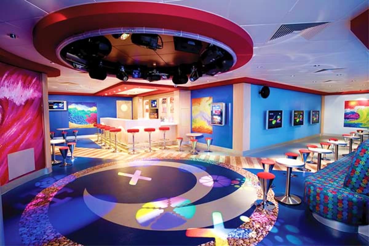 Modern cruise ship entertainment venue with blue walls, red circular ceiling feature, illuminated dance floor with colorful g