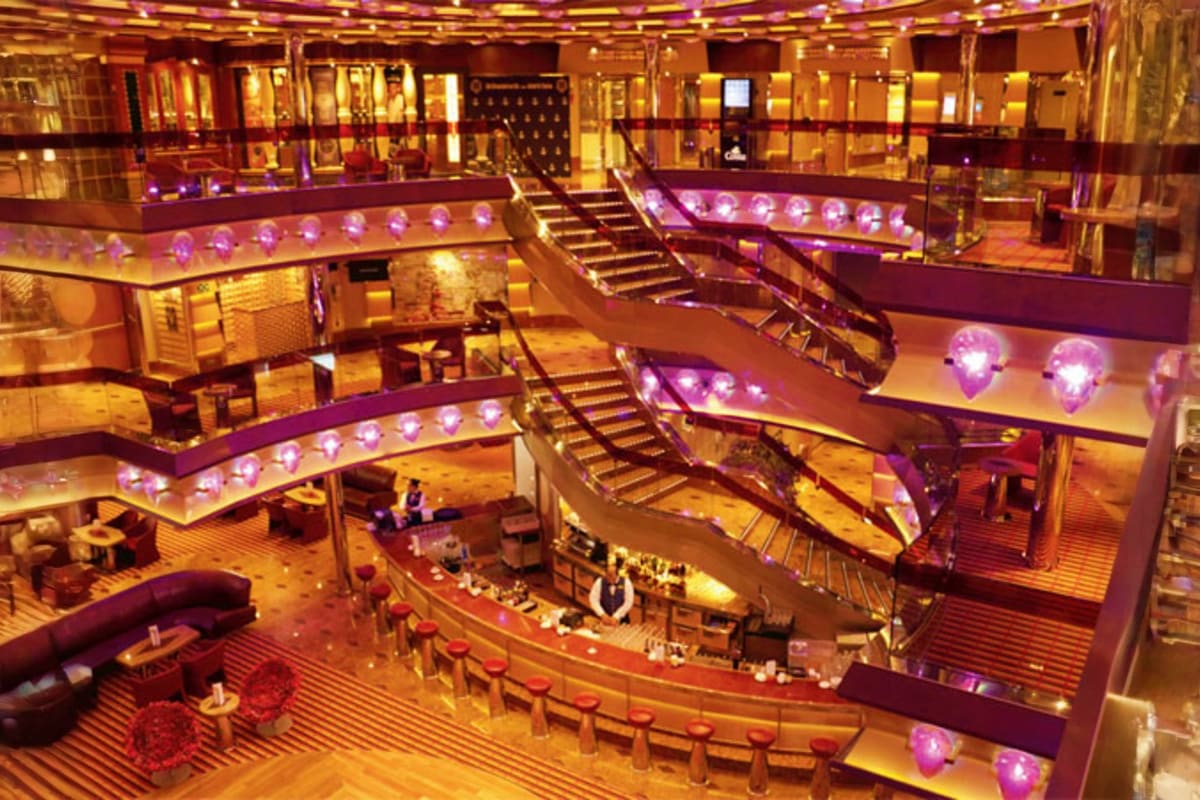 Luxury cruise ship interior atrium with multiple curved deck levels, grand staircase, purple ambient lighting, and elegant go
