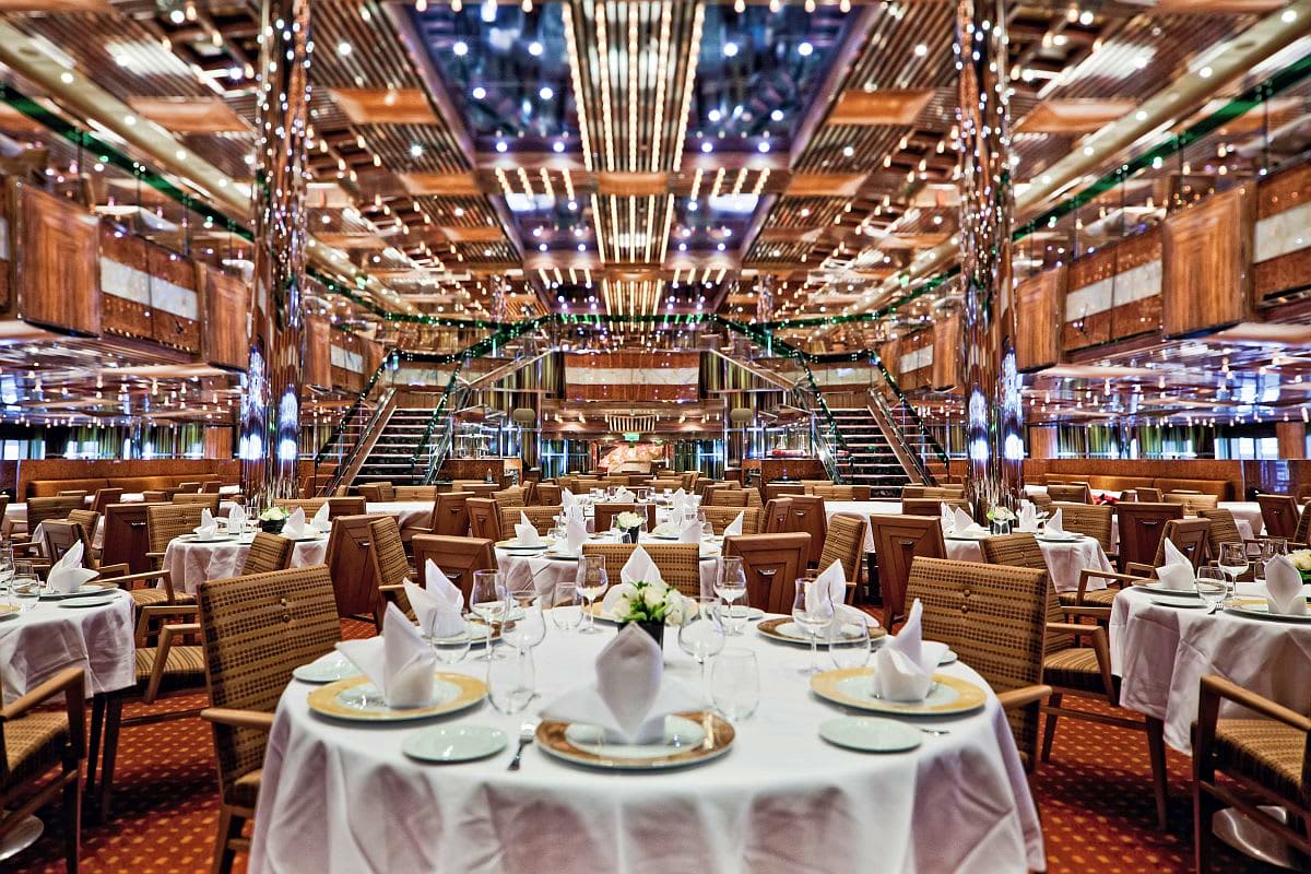 Elegant main dining room of Costa Fascinosa cruise ship with round tables, white linens, and ornate ceiling lighting